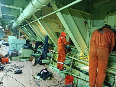 Cleaning crew in orange coveralls working in a ship's engine room