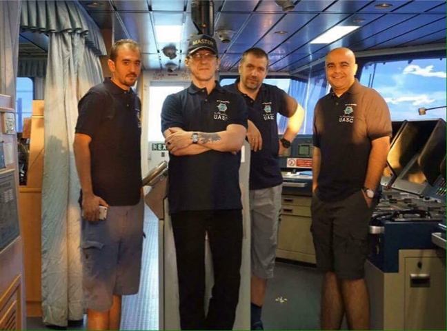 Four officers on a ship's bridge in matching UASC polo shirts